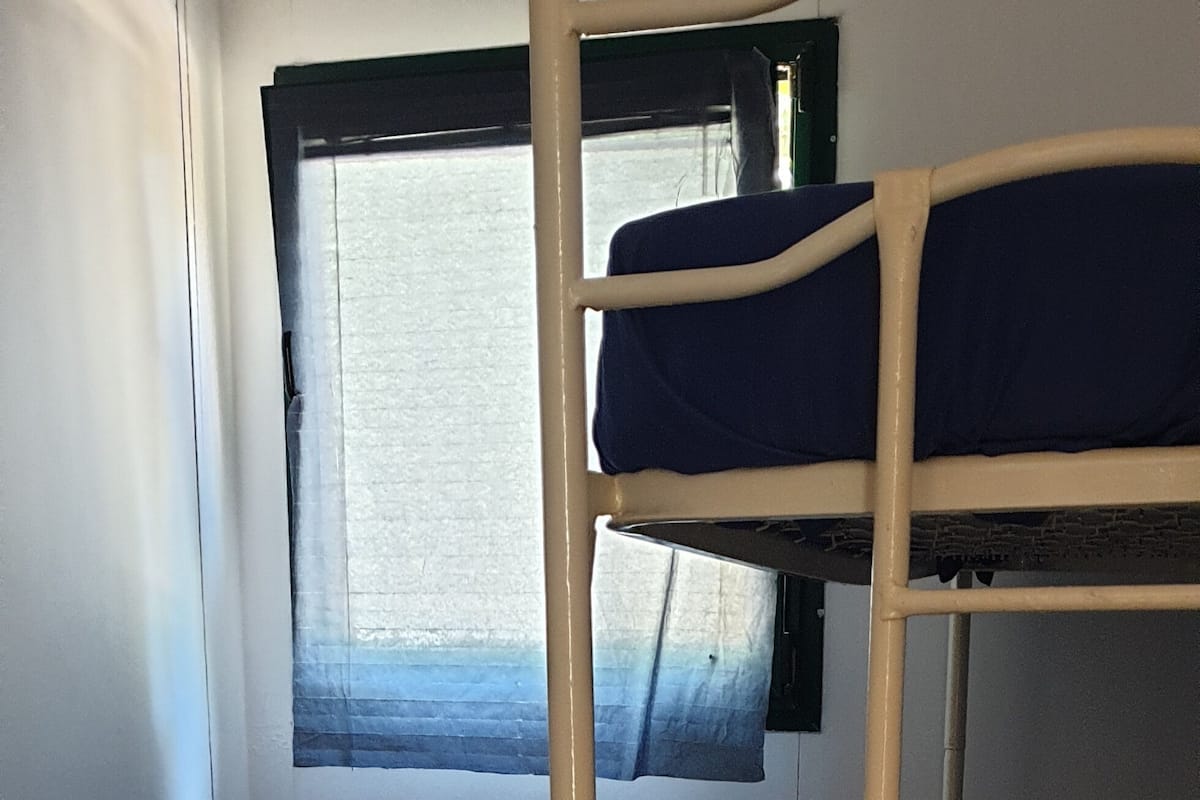 A bunk bed room with a window, a bed on the left, and a bunk bed on the right.