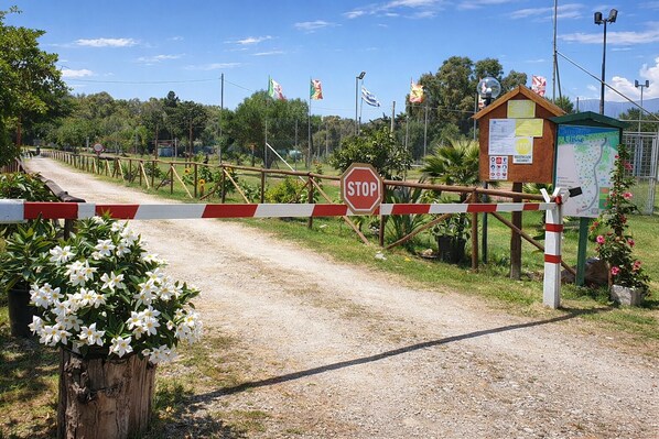 Una entrada con portón, una señal de stop, una estructura de madera con carteles informativos y un mapa.