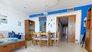 A living room with a sofa, a dining table with chairs, a wooden cabinet, and a hallway leading to another room. - Lovely apartment for 4 people with A/C, WIFI, TV and terrace (Torroella De Montgrí)