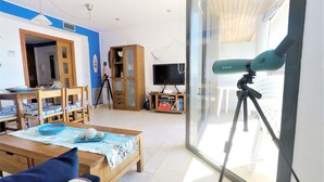 A living room with a telescope on a tripod, a television, and a dining area with chairs and a table. - Lovely apartment for 4 people with A/C, WIFI, TV and terrace (Torroella De Montgrí)