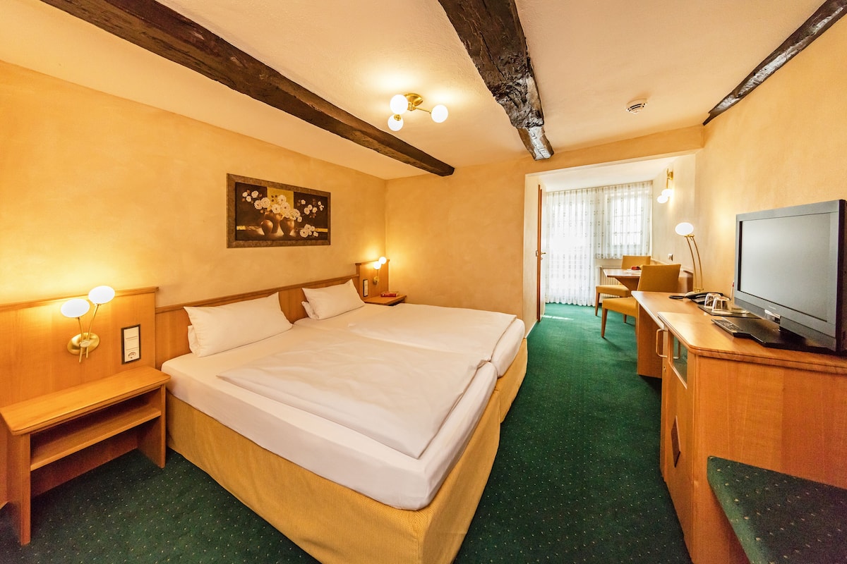 A hotel room with a large bed, bedside tables, a desk with a television, and a painting on the wall.