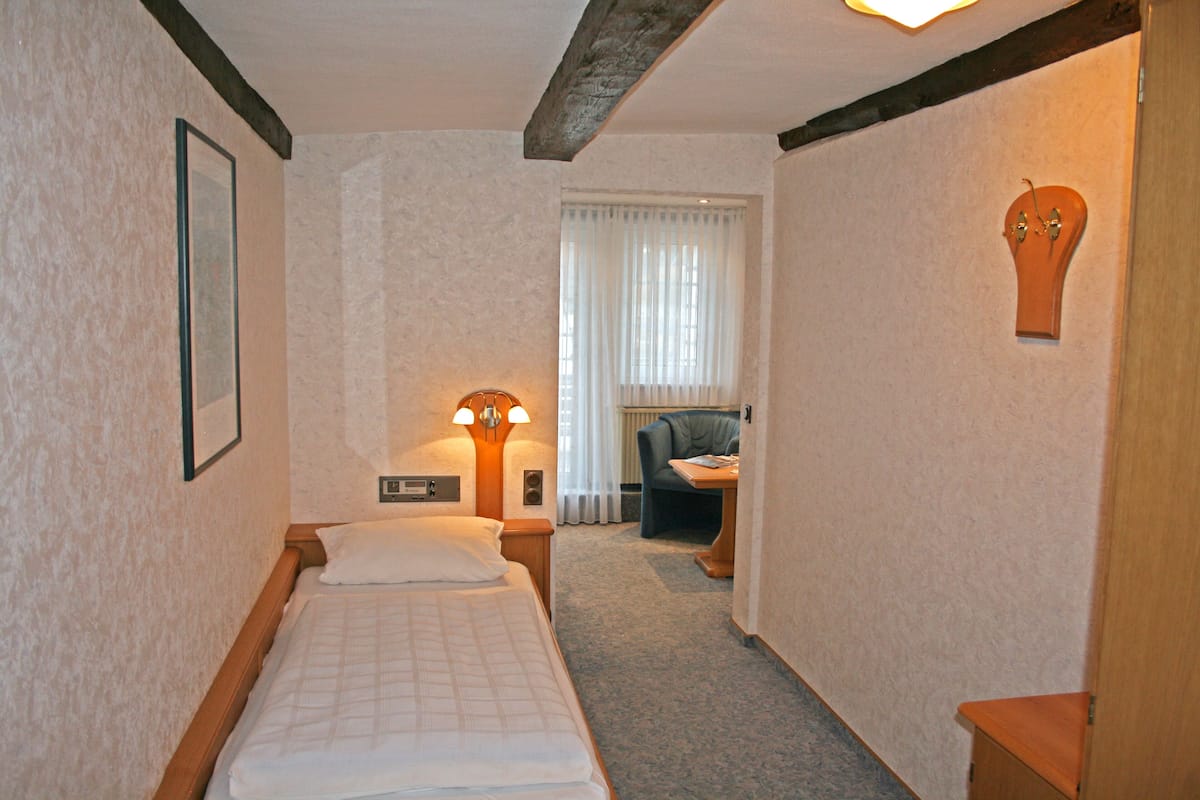 A hotel room with a bed, a desk, a chair, and a lamp.