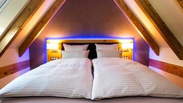 Un dormitorio con techo inclinado, vigas de madera y una cama con ropa de cama blanca.