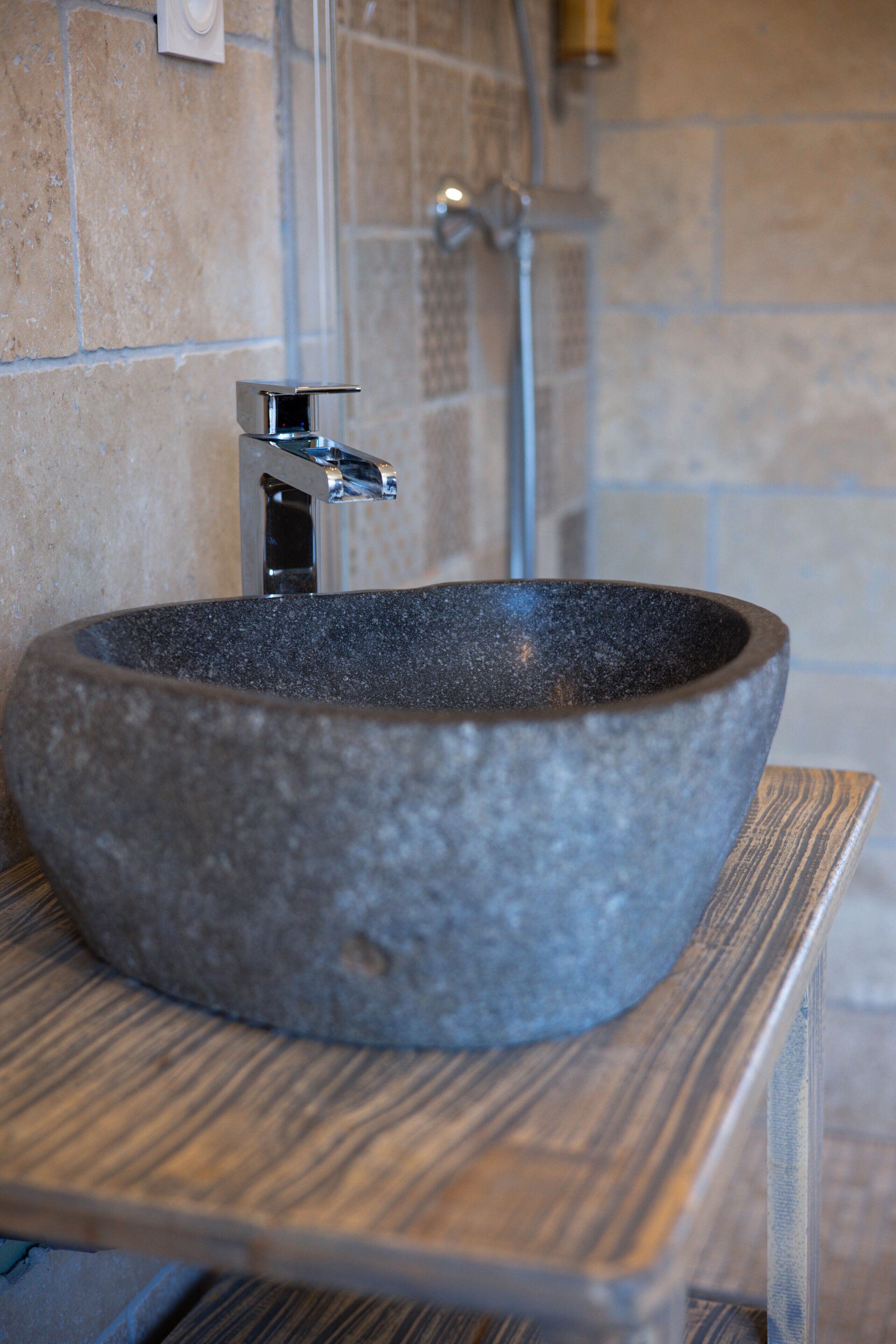 Un évier en pierre avec un robinet moderne, installé sur une plateforme en bois dans une salle de bain aux murs carrelés.