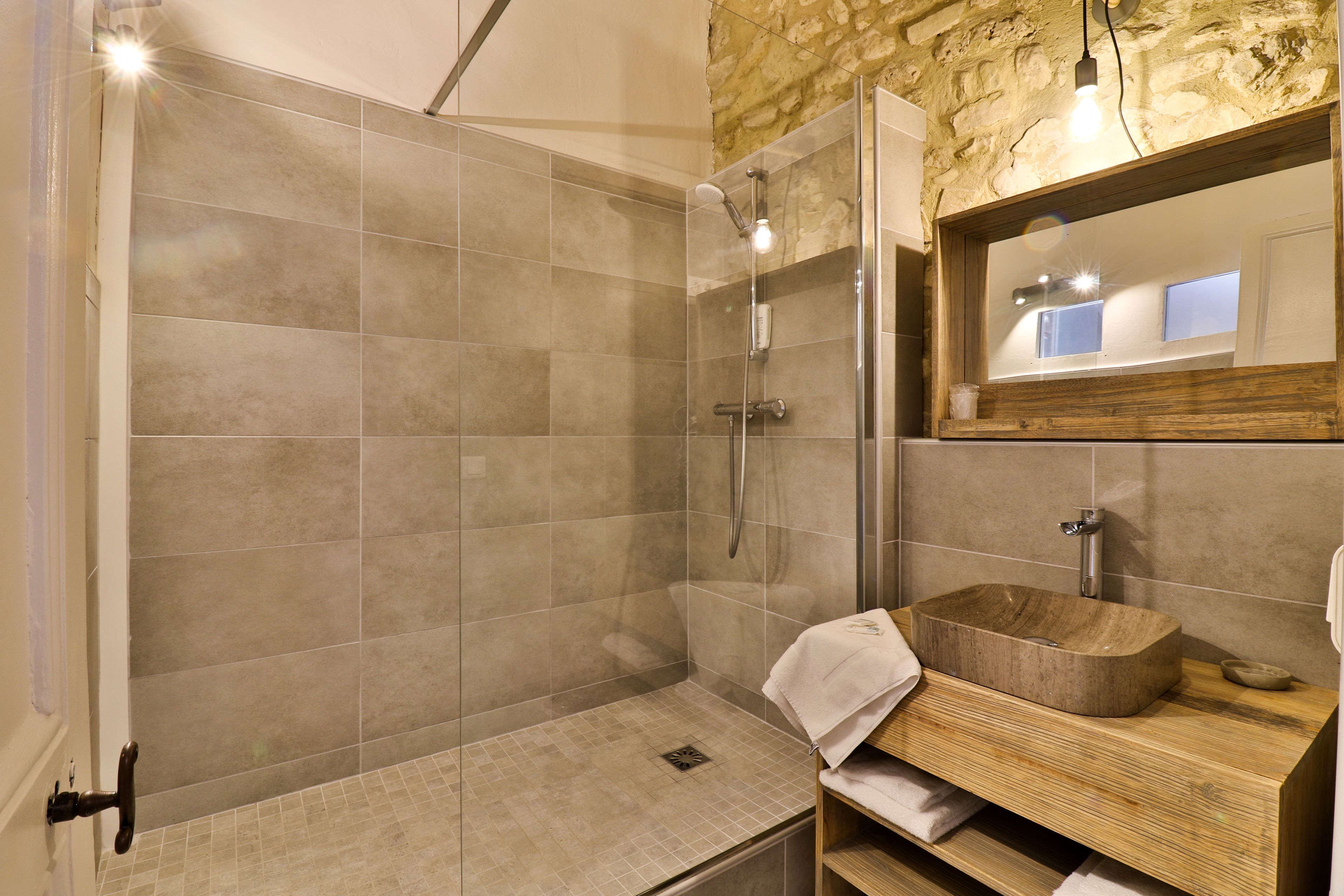 A modern bathroom with a glass-enclosed shower, a wooden vanity, and a stone accent wall.