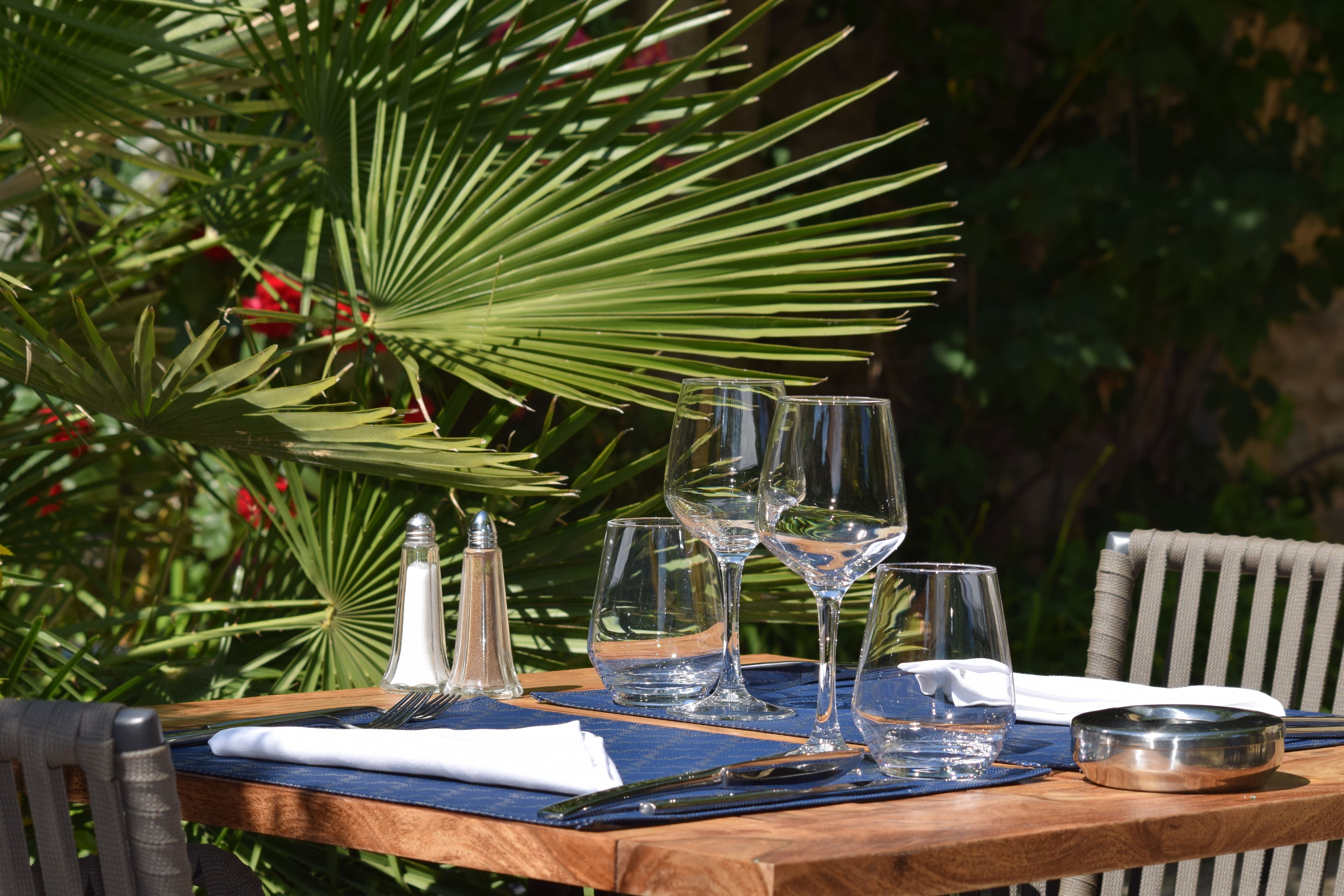 Une table en bois, installée à l’extérieur, avec de la vaisselle transparente, un salier et une serviette.