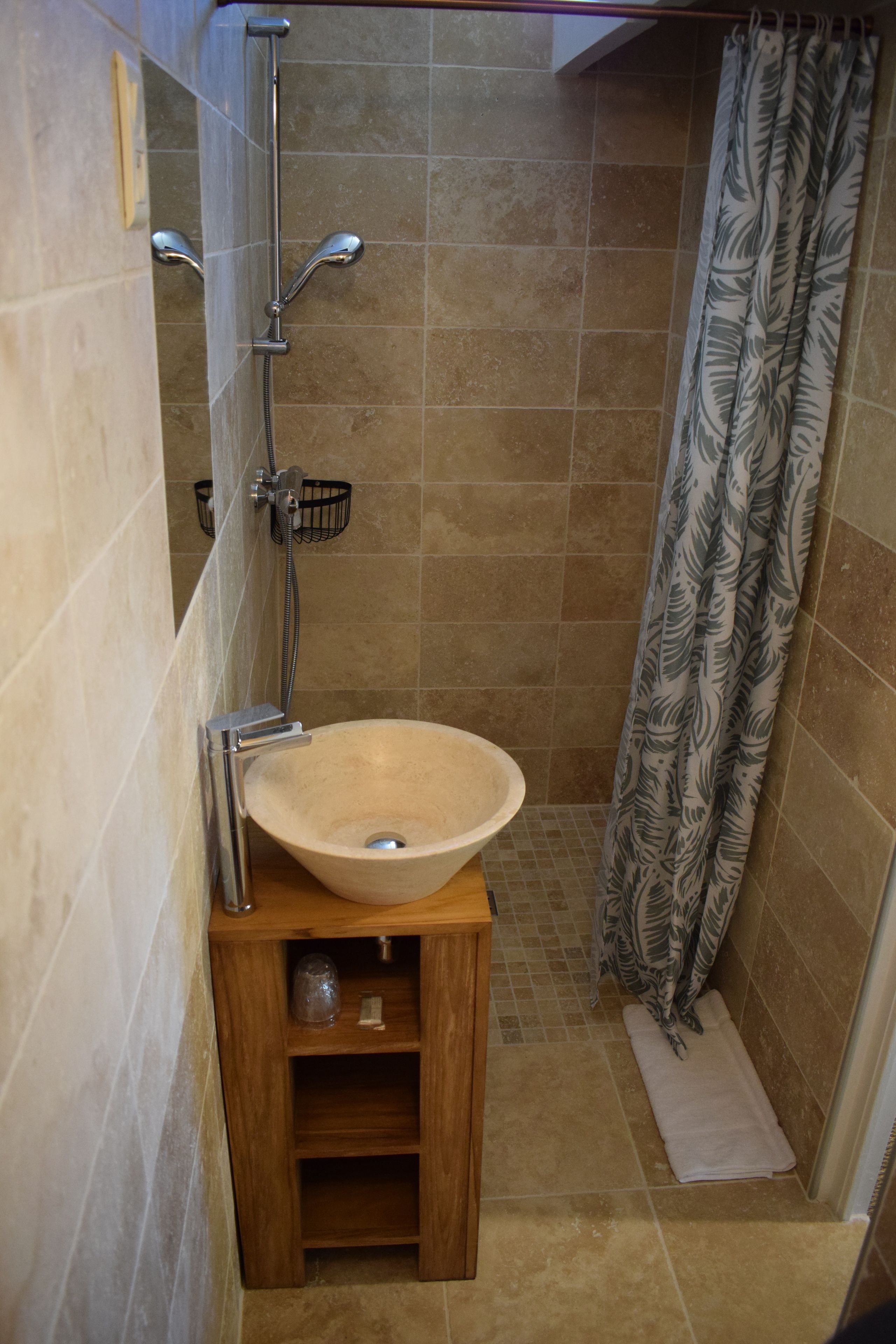 Une salle de bain avec un lavabo beige, une douche et un rideau de douche à motifs.