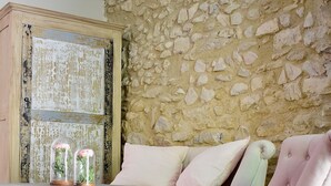 A room with a stone wall, a wooden table with a glass top, and a pink upholstered chair. - La Bastide Bleue (Seguret)