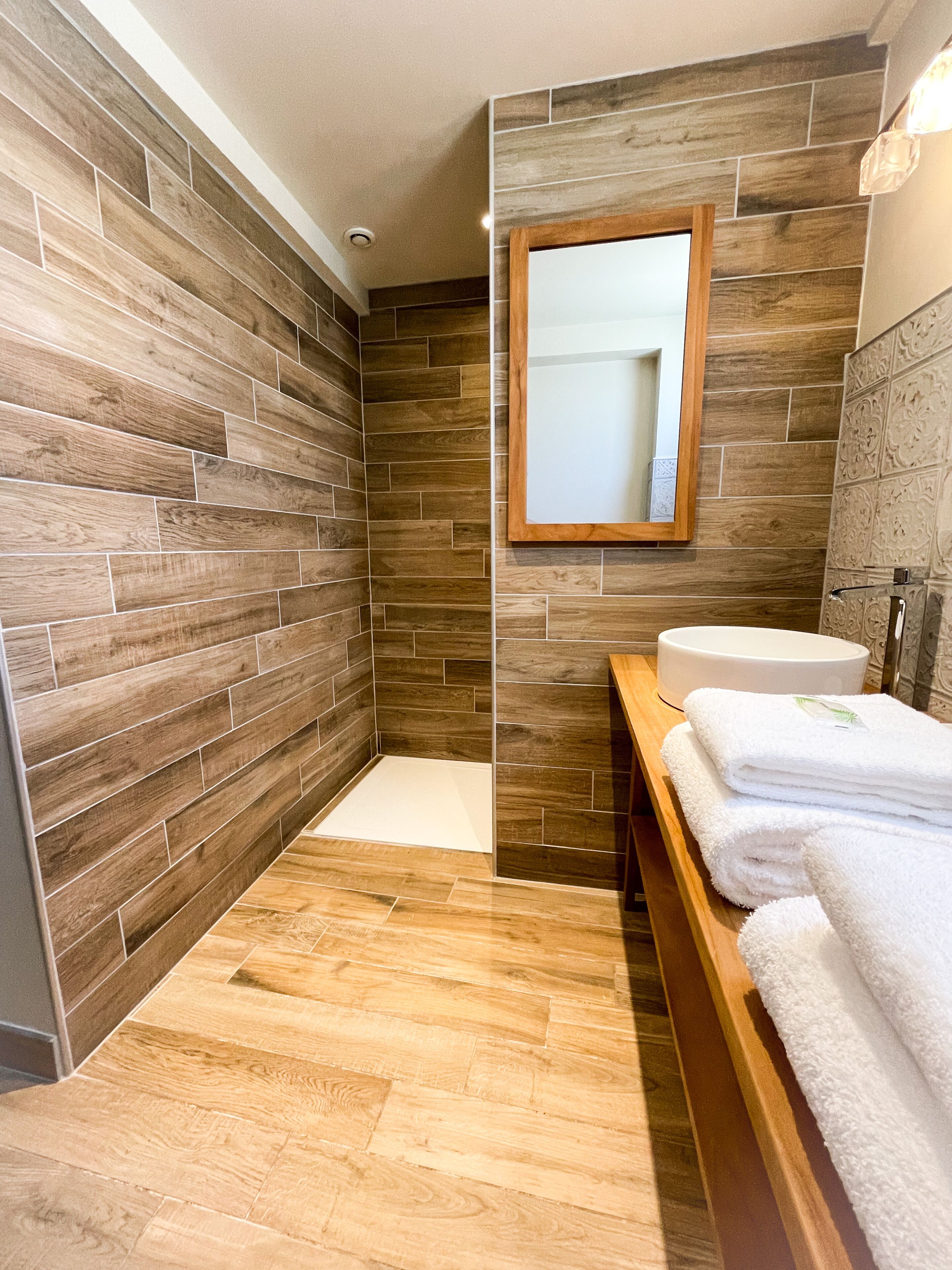 A modern bathroom with wooden wall tiles, a wooden bench with towels, and a white sink.