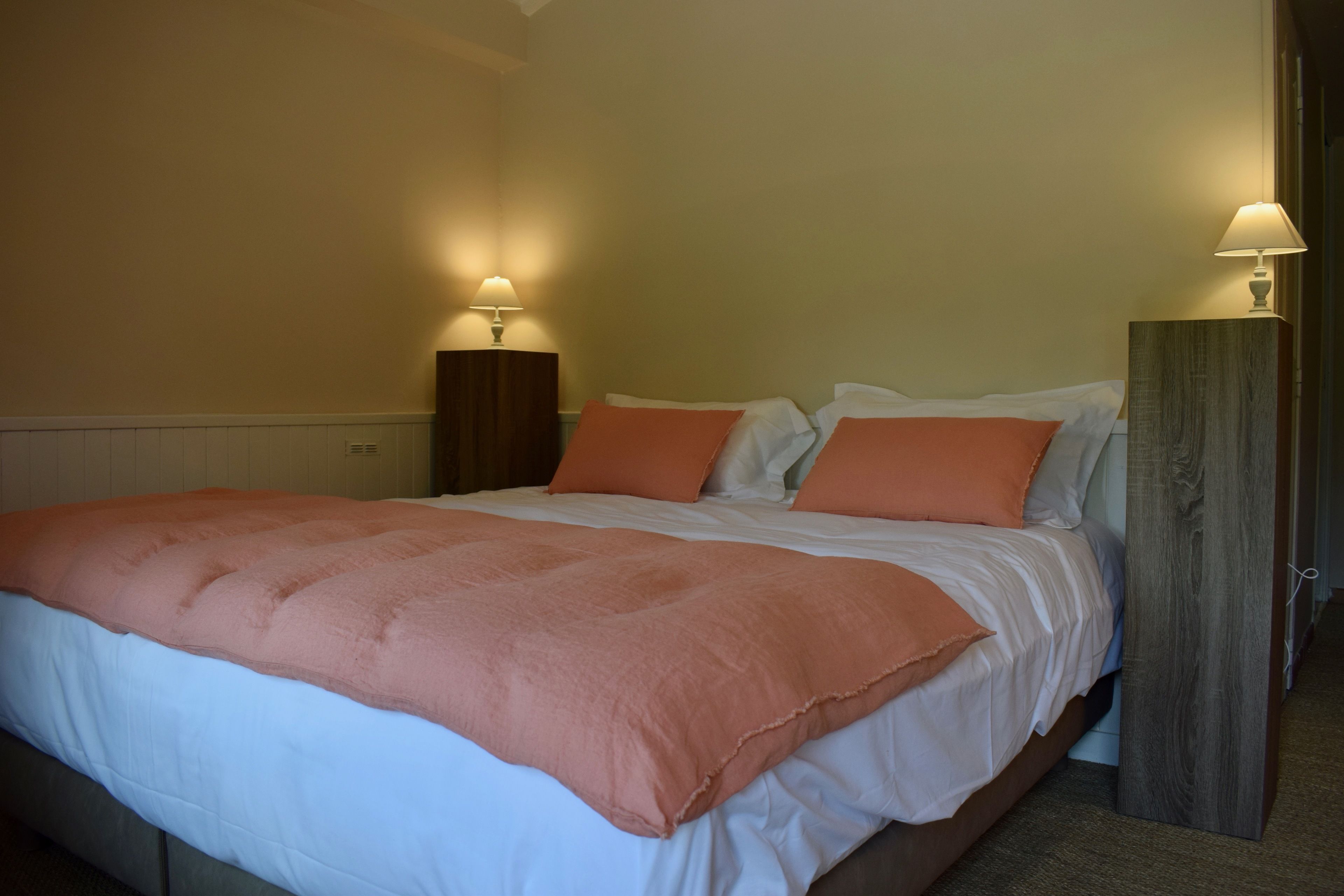 A neatly made bed with a pink blanket and white sheets, flanked by two bedside lamps on wooden nightstands.