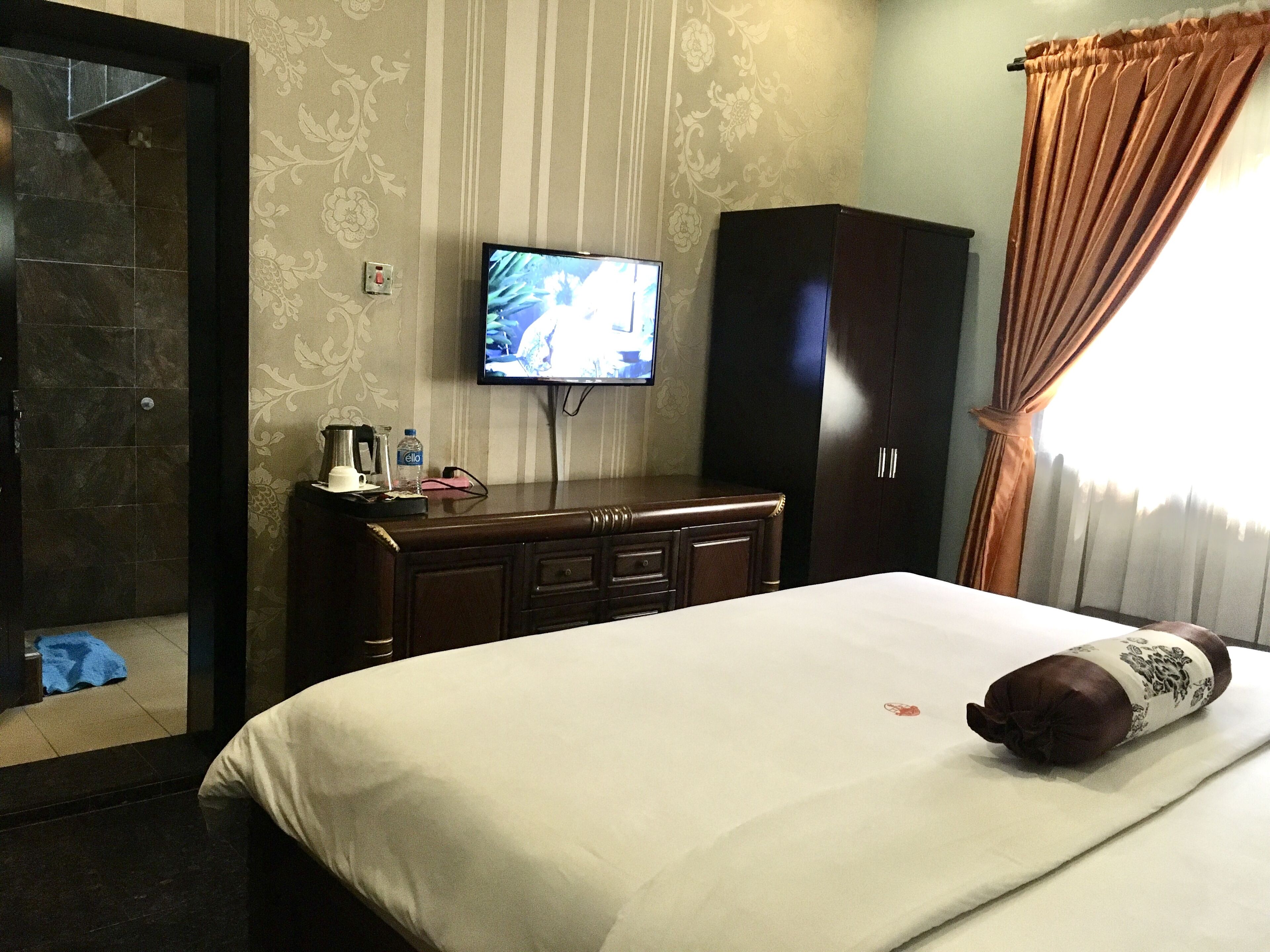 Habitación de hotel con cama, televisor montado en la pared, armario y baño con ducha.