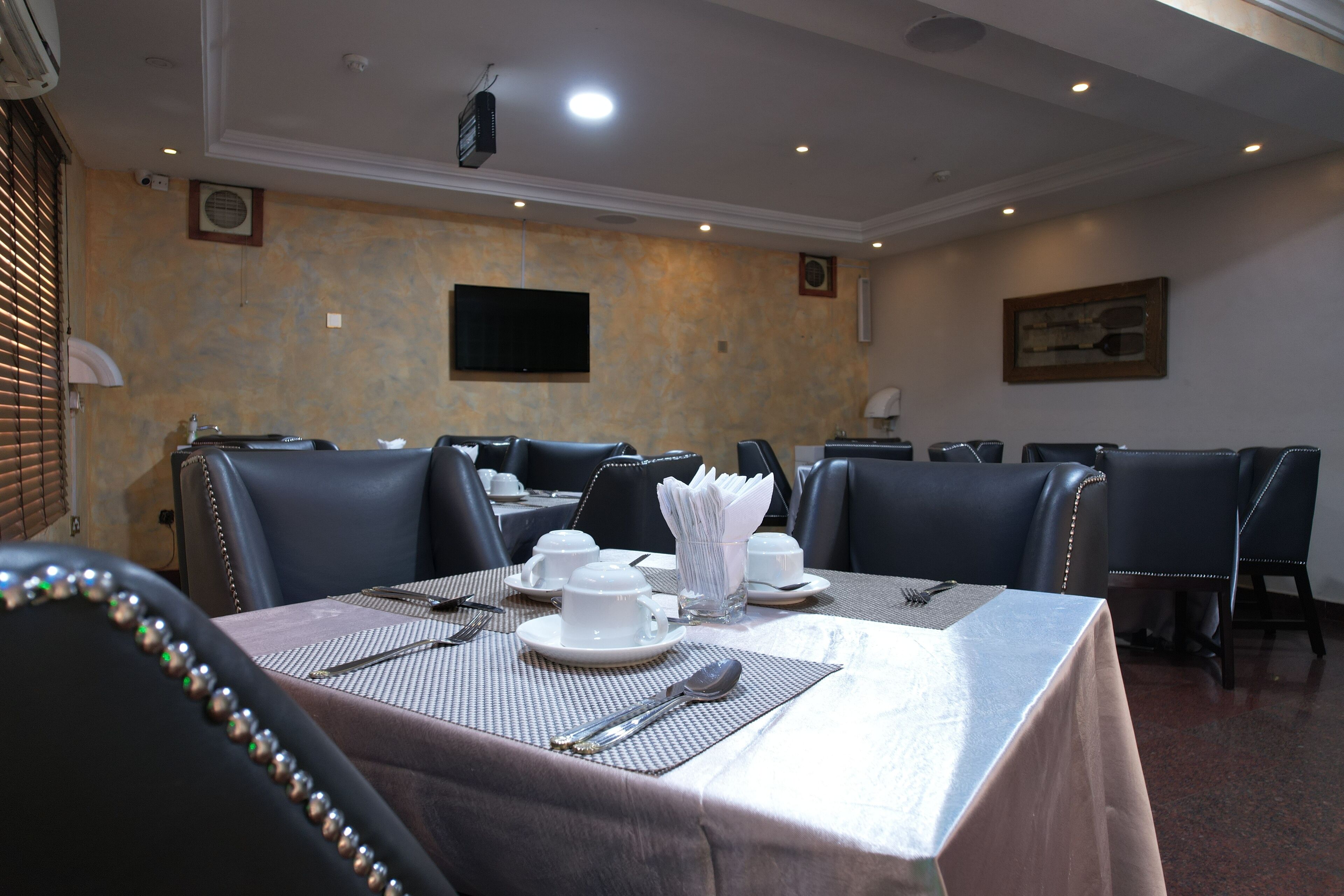 A conference room with a table set for a meeting, equipped with a projector, a flat-screen TV, and a framed picture on the wall.