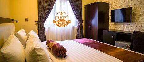 A hotel room with a bed, pillows, a TV, and a wardrobe.