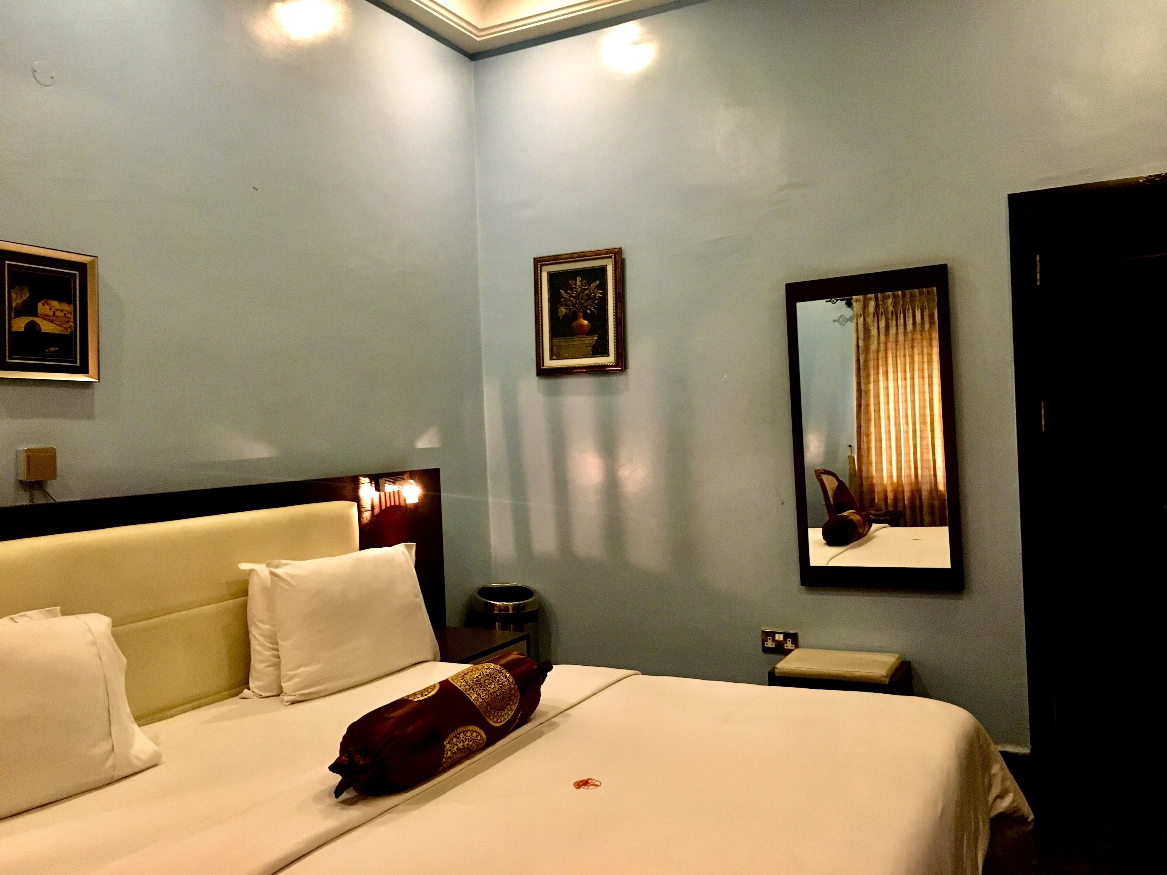 A hotel room with a bed, a nightstand, a mirror, and a framed picture on the wall.
