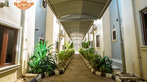 A corridor with a covered walkway, flanked by plants and buildings. - IBD International Hotels Limited (Abeokuta)
