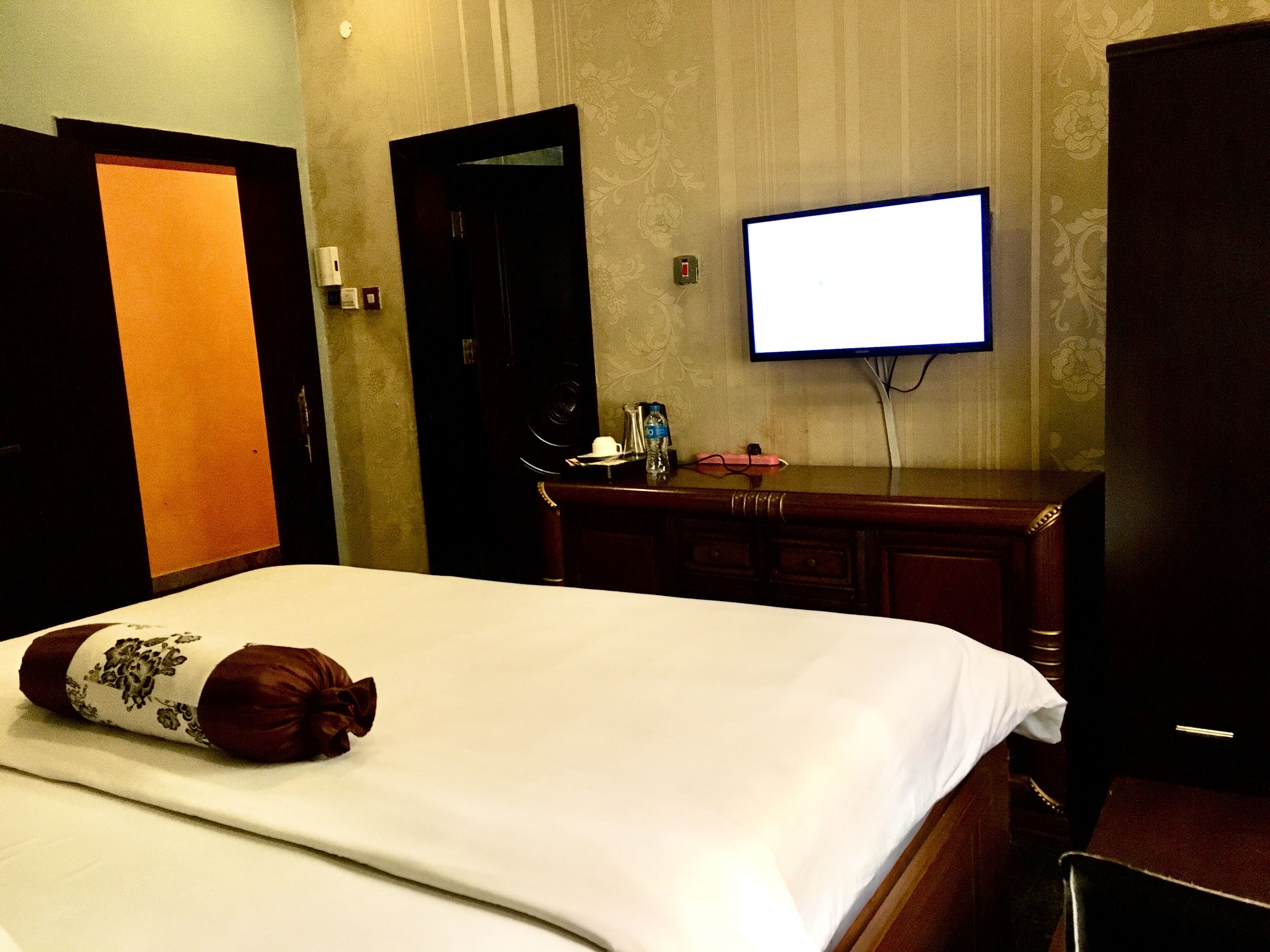 Une chambre d’hôtel avec un lit, un téléviseur fixé au mur, une commode et une porte.