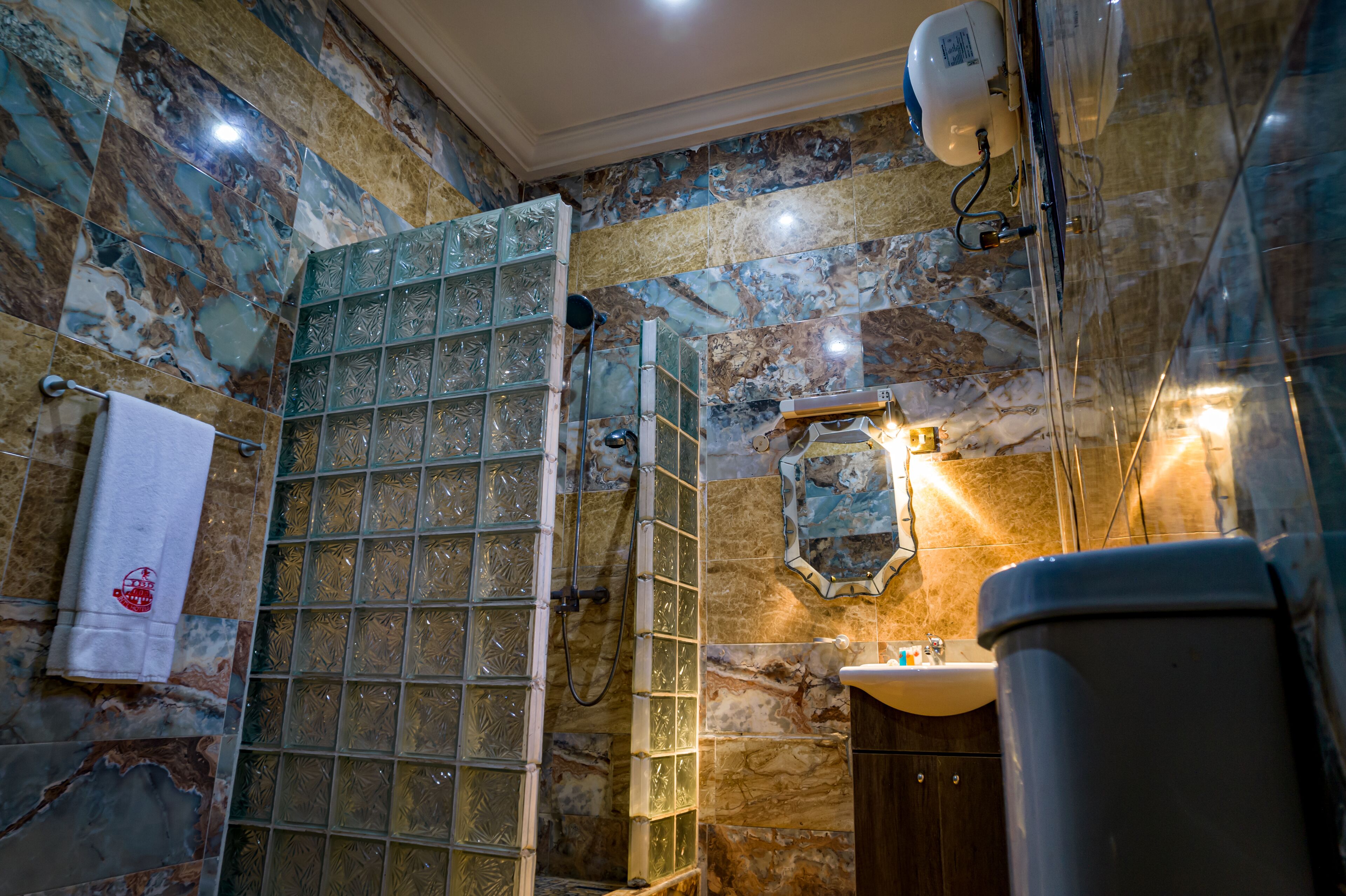 A bathroom with a glass shower enclosure, marble walls, a sink, and a towel rack.