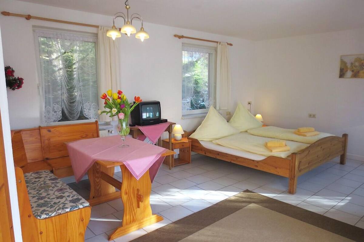Een knus slaapkamer met een houten bed, een klein bureau met een roze tafelkleed, een televisie en een raam met gordijnen.