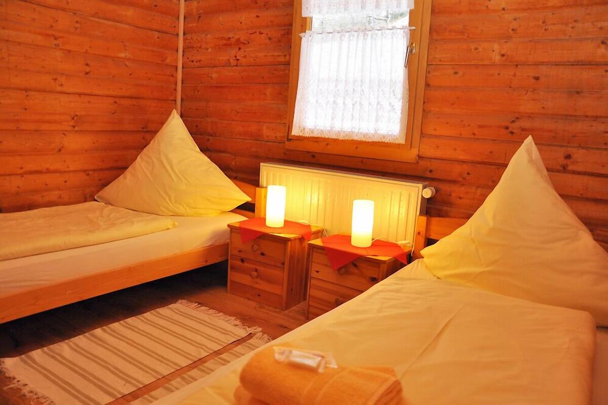 Een gezellig houten kamer met twee eenpersoonsbedden, een klein nachtkastje met twee lampen en een raam met kantgordijnen.