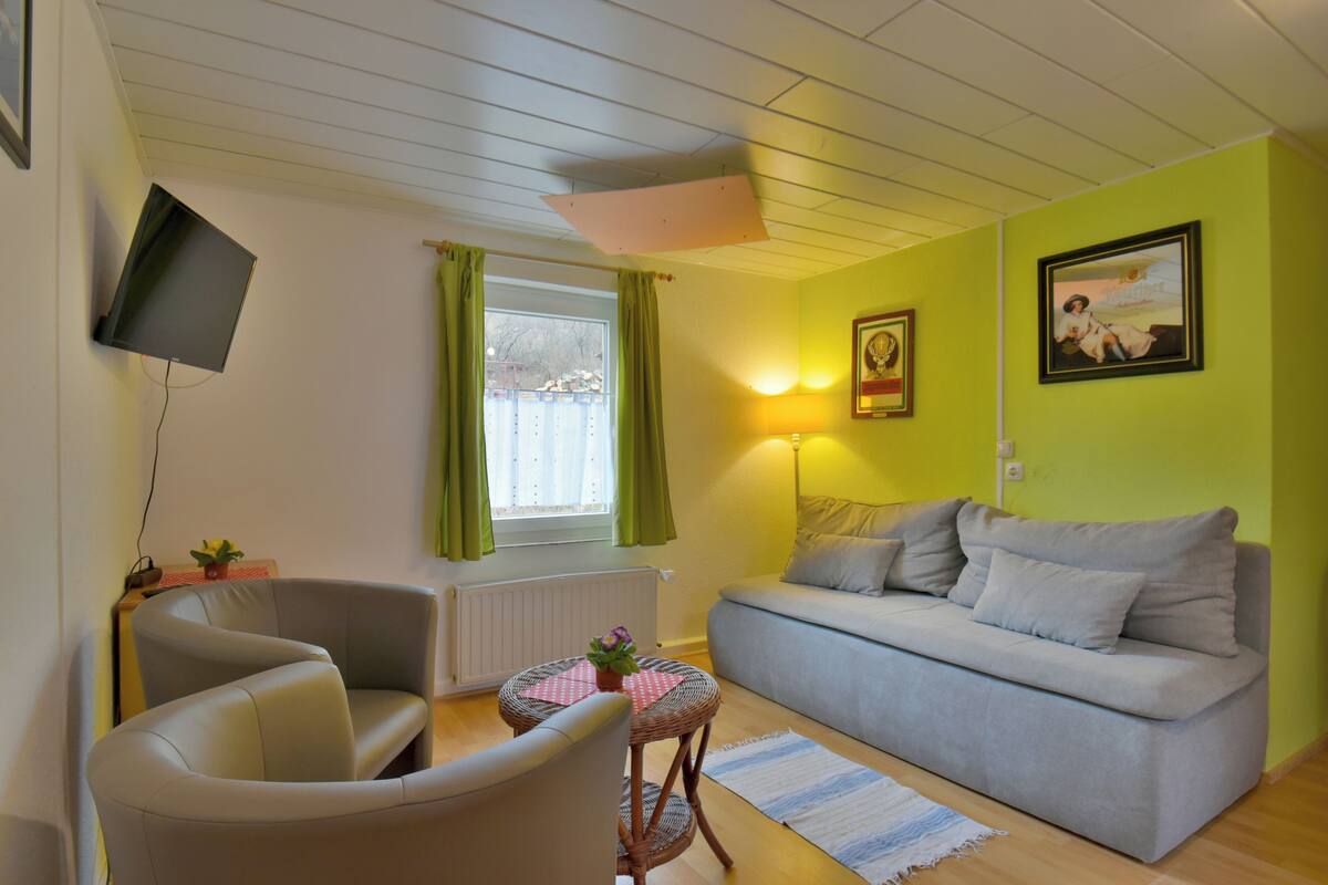 Een woonkamer met een bank, fauteuil en een bijzettafeltje met een plant.