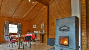 A wooden interior with a stone fireplace, a dining table with chairs, and a window with curtains.