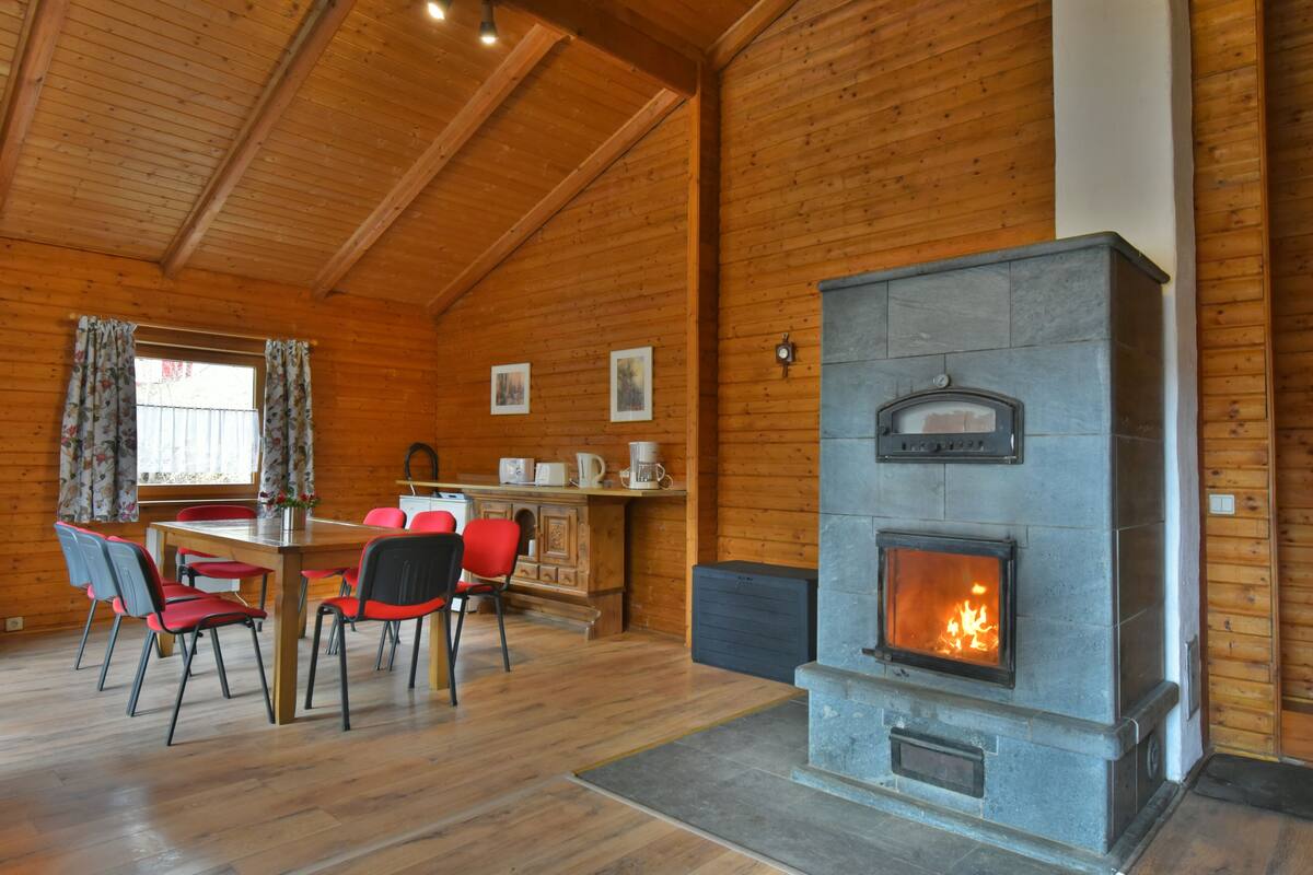 Een houten interieur met een stenen open haard, een eettafel met stoelen en een raam met gordijnen.