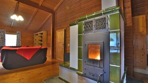 A wooden interior with a wood-burning stove, a bed with a red blanket, and a wooden ceiling.