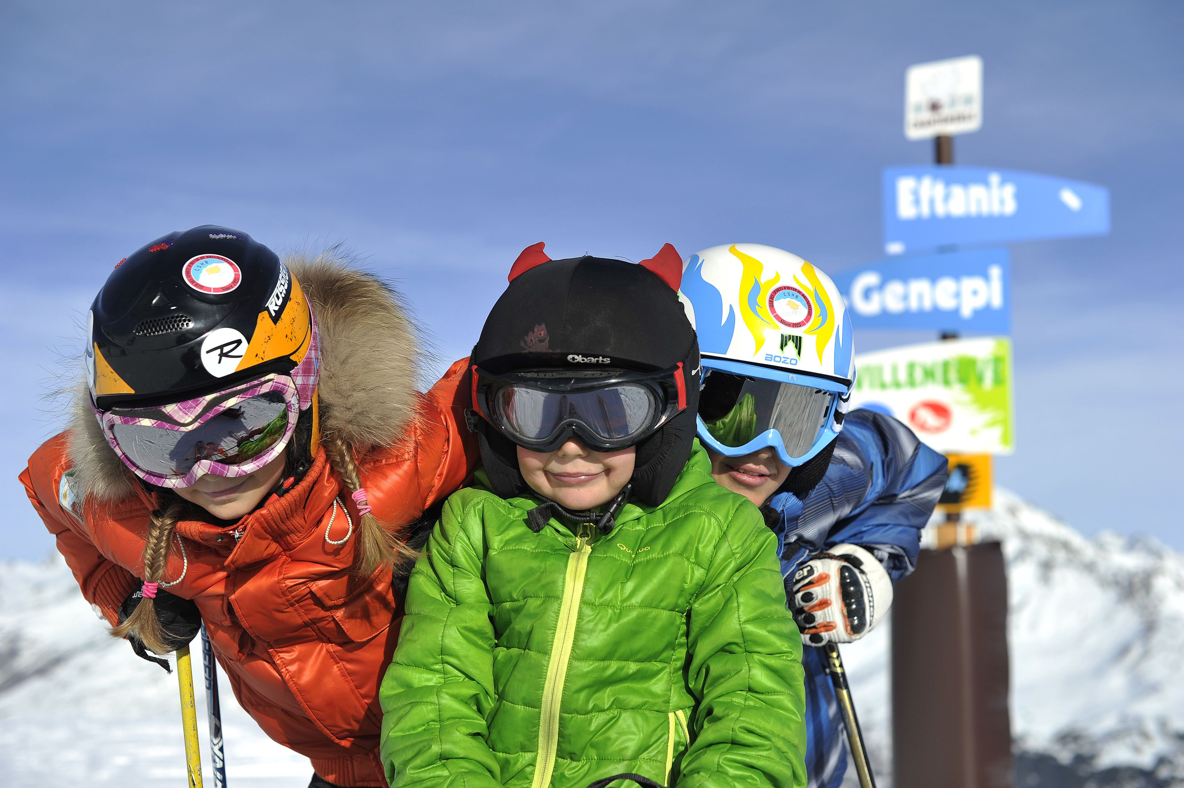 A group of skiers with helmets and ski poles, standing in front of a sign with directions.