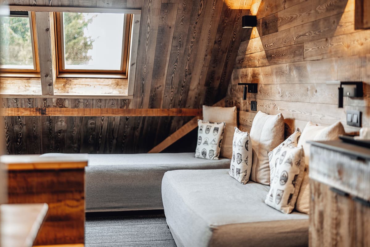 Ein gemütliches Zimmer mit Holzvertäfelung, einer Couch mit gemusterten Kissen und einem Fenster, das natürliches Licht hereinlässt.