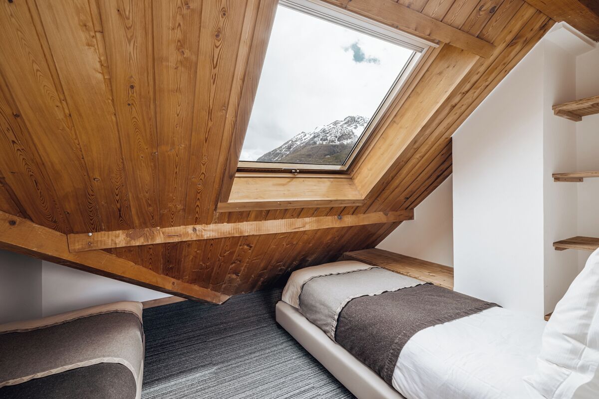 A room with a sloped ceiling, wooden beams, a skylight, a bed, and a small seating area.