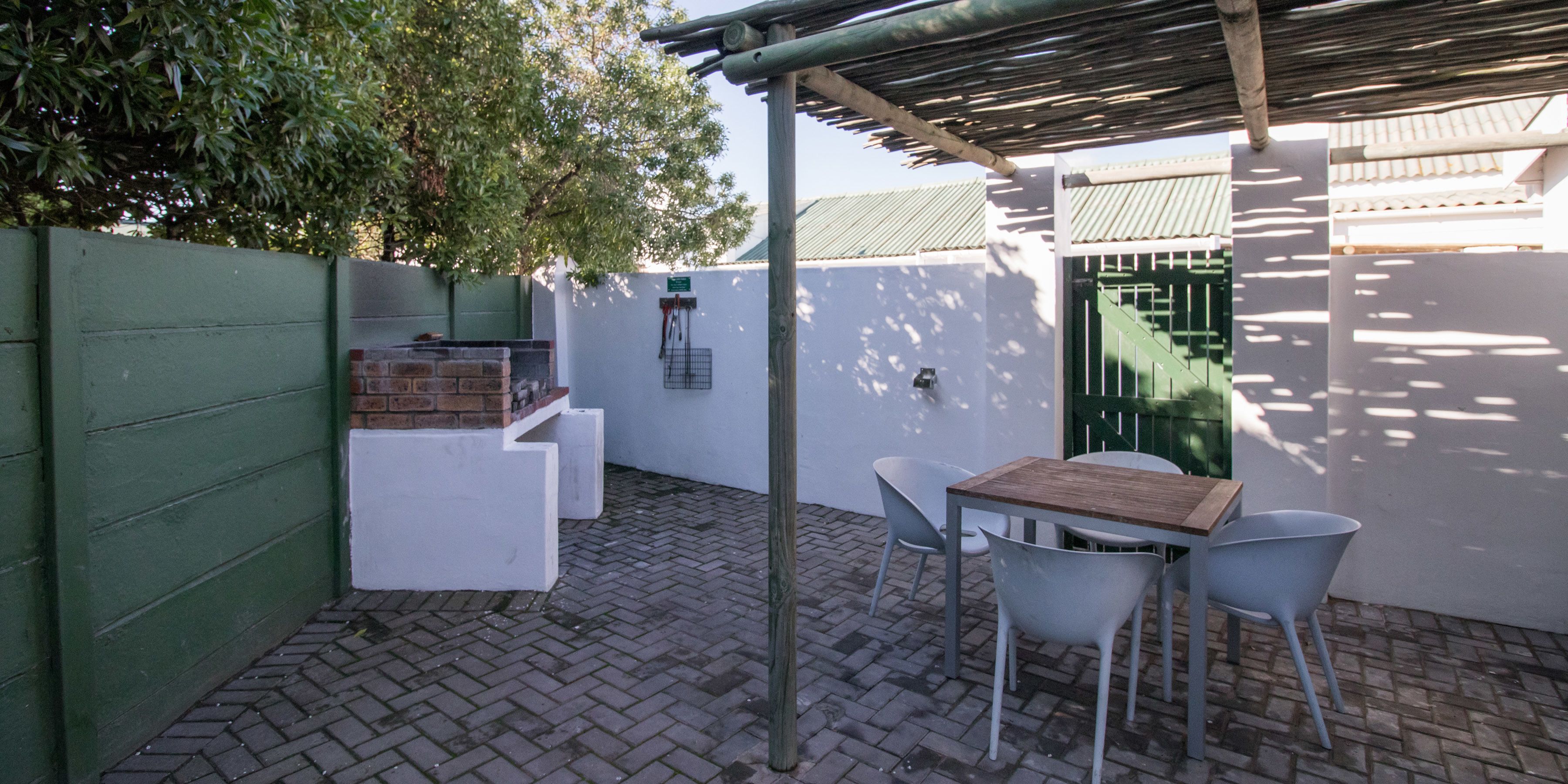 A patio area with a brick floor, a wooden table, and white chairs.