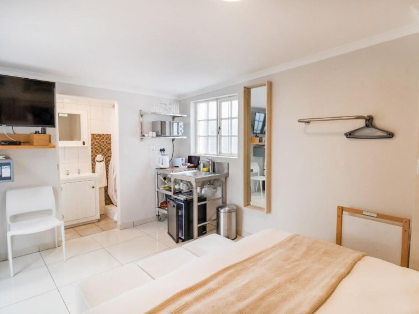 A hotel room with a bed, a desk with a chair, a kitchenette, a TV, and a mirror.