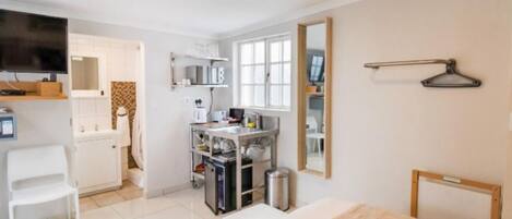 A hotel room with a bed, a desk with a chair, a kitchenette, a TV, and a mirror.