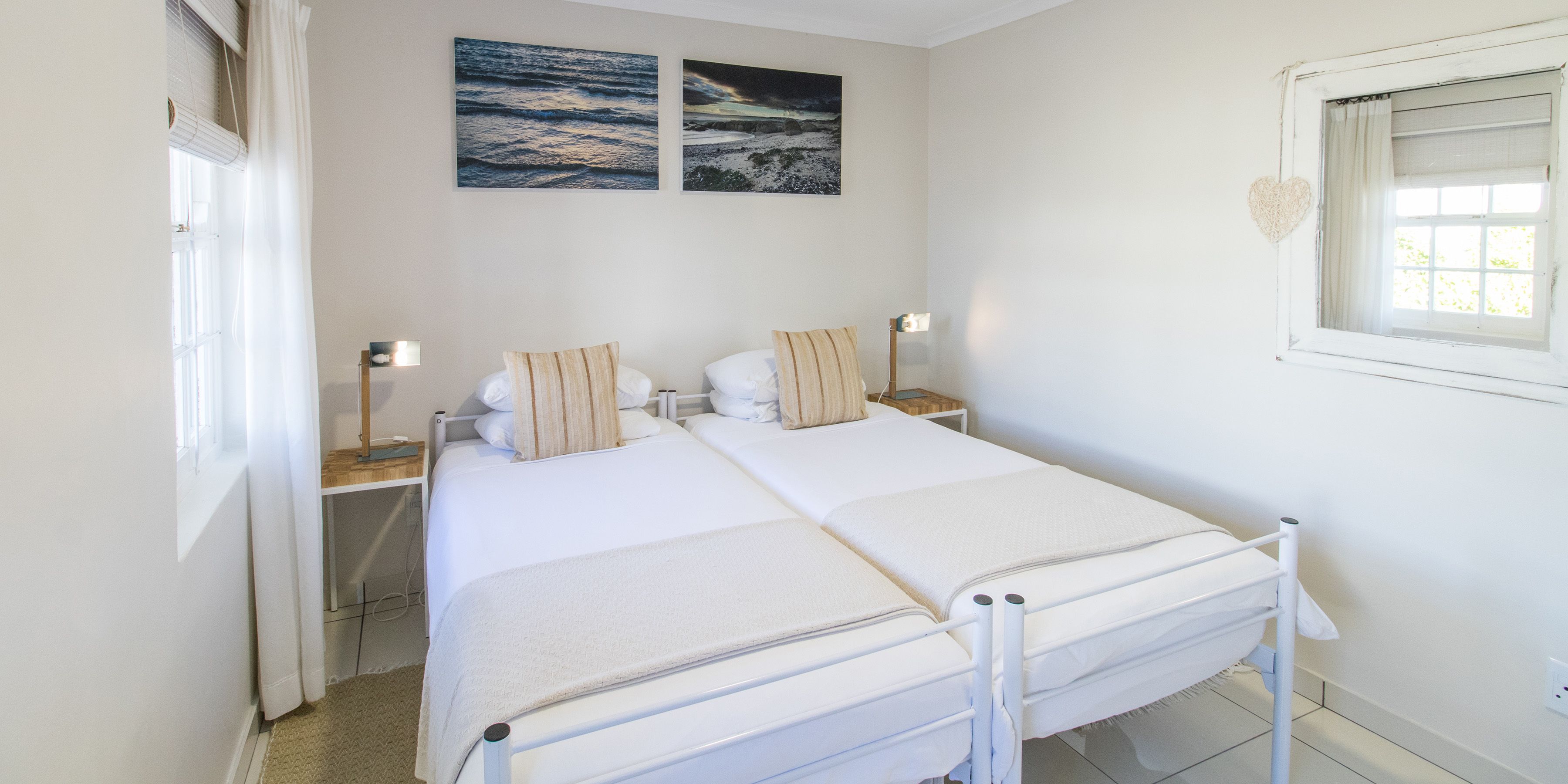 A double bed with white bedding, two bedside tables with lamps, and two wall-mounted paintings.