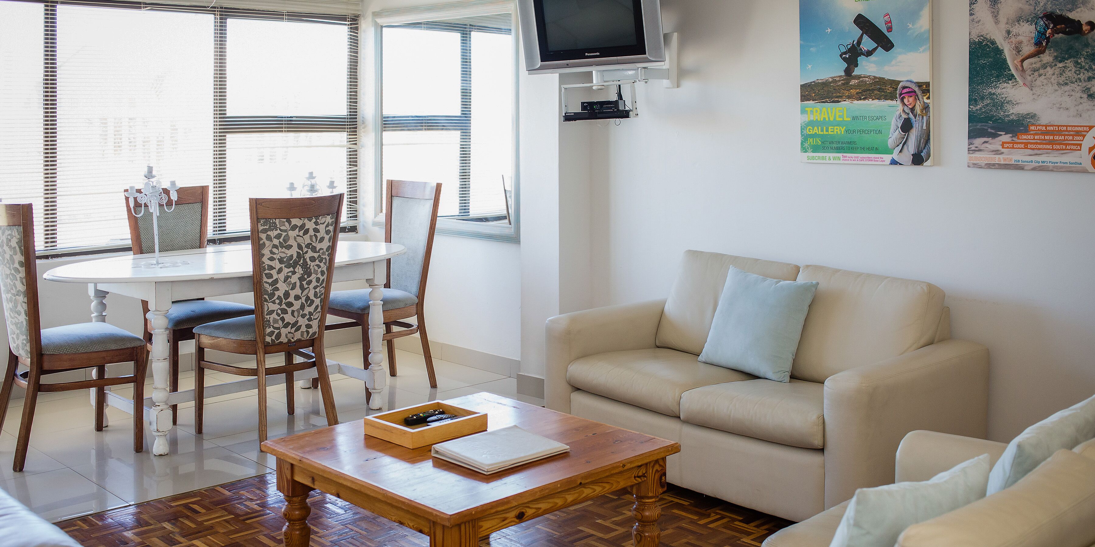 A living room with a beige sofa, a wooden coffee table, and a dining area with a white table and patterned chairs.