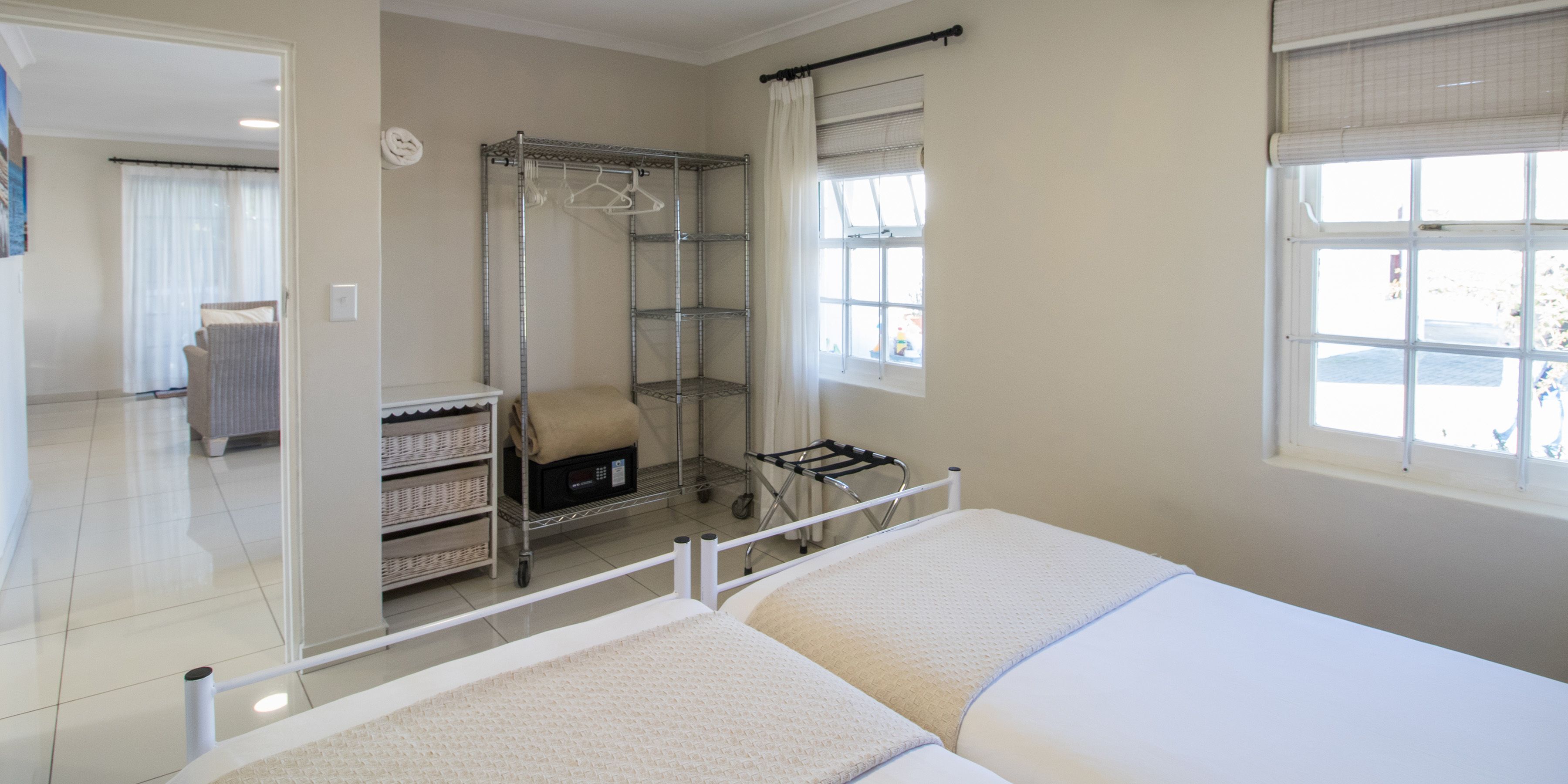 A clean, well-lit room with a large mirror, a metal shelving unit with baskets, a chair, and a window with curtains.