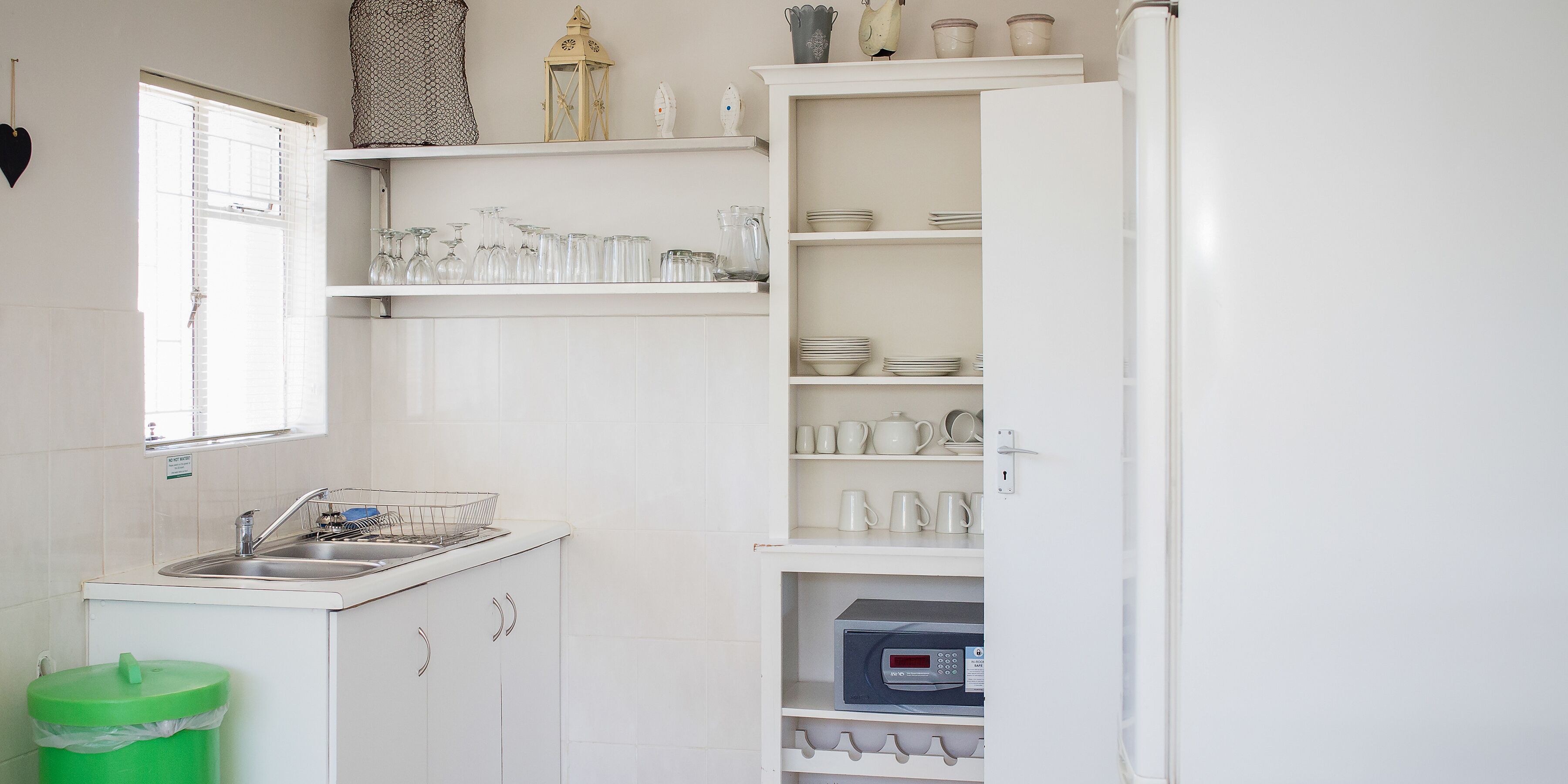 Una cocina con armarios blancos, un fregadero y un cubo de basura verde.