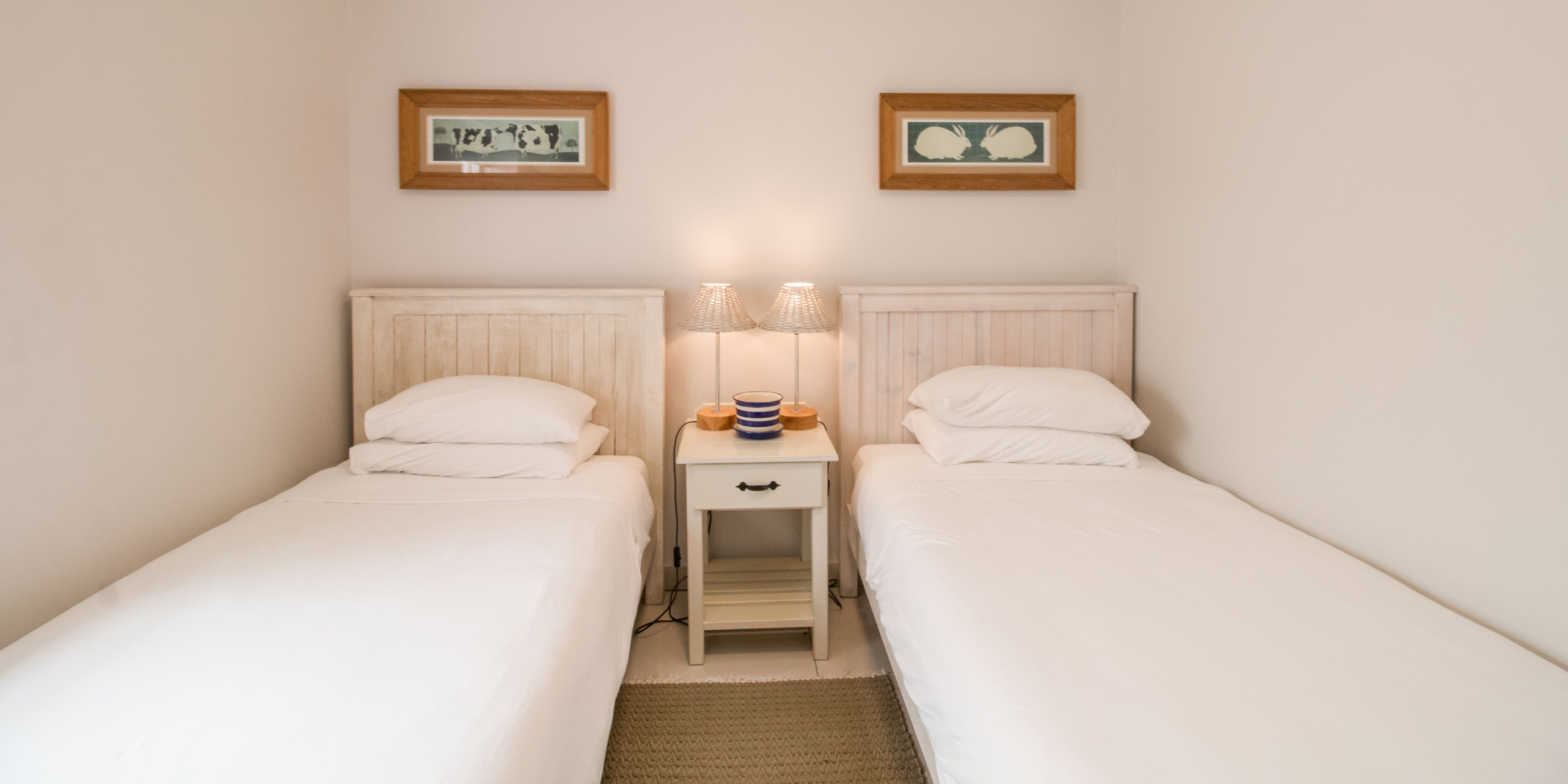 A twin room with two single beds, a bedside table with lamps, and two framed pictures on the wall.