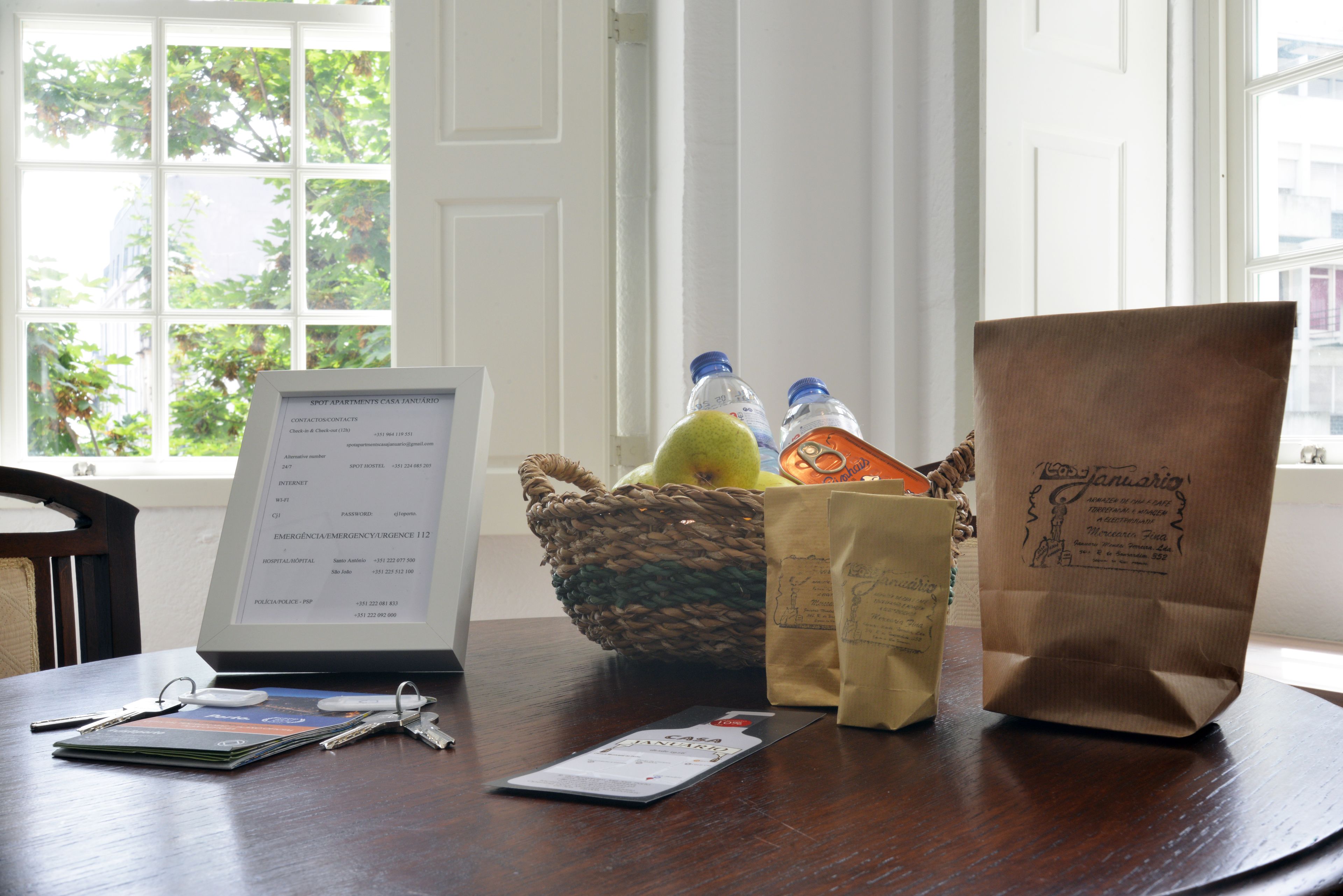 Una mesa de madera con una computadora portátil, llaves, una billetera y una cesta que contiene botellas y una bolsa de papel marrón.