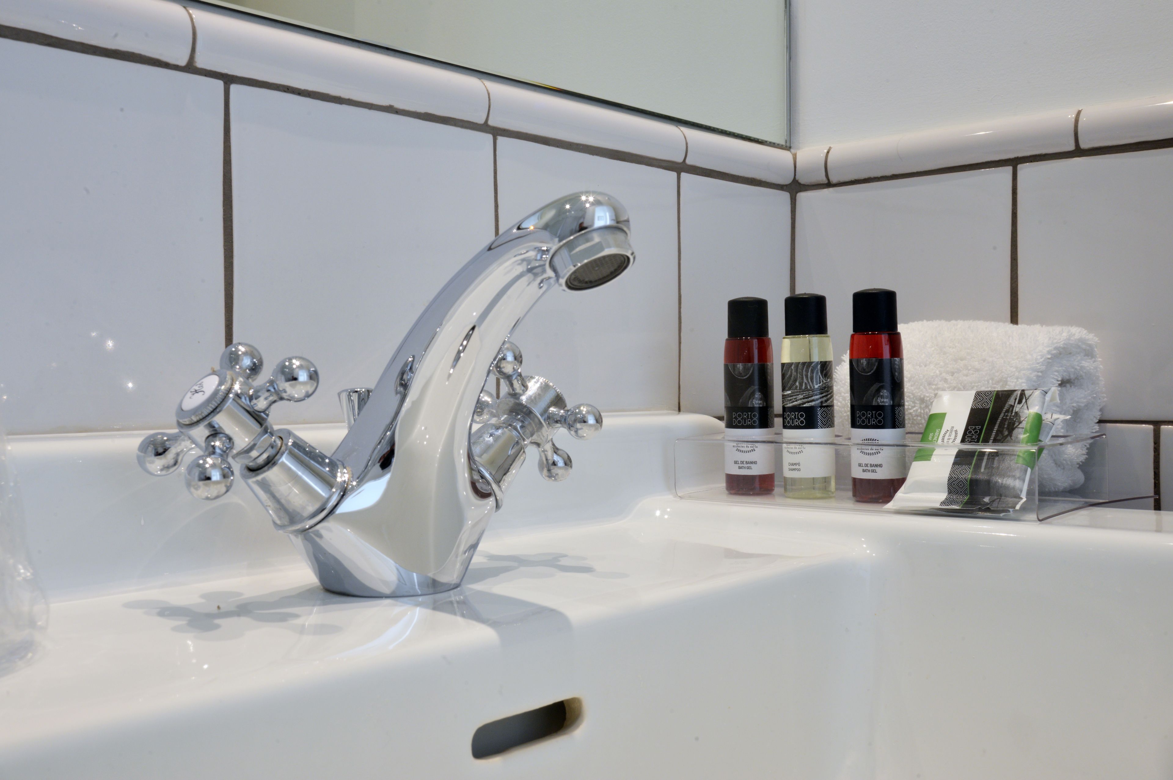 Casa de banho com torneira de metal cromado, lavatório branco e artigos de higiene pessoal, incluindo champô e gel de banho.