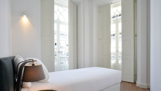 A minimalist bedroom with a white bed, a green side table, and a lamp. - Spot Apartments Casa Januario (Porto)