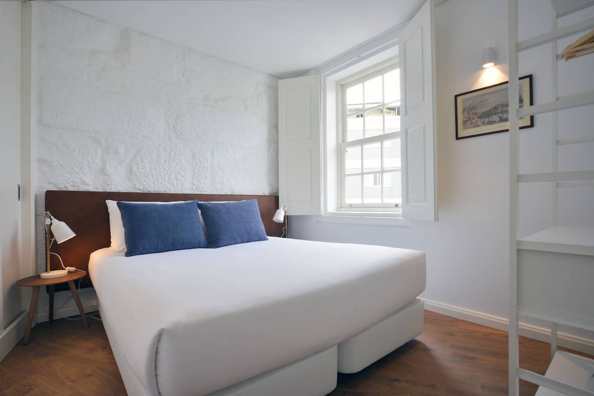 A bedroom with a large bed, a nightstand, a lamp, a window, and a framed picture on the wall.