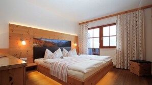 A wooden bed with a headboard, a bedside table, a window with curtains, and a wall-mounted TV. - Edelweiss - Wiesenhof (Kaunerberg)
