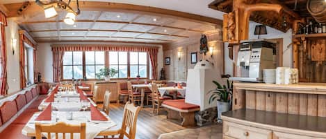 A restaurant with wooden interiors, a long communal table, and a kitchen area.
