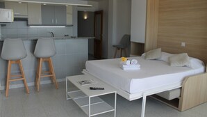 Een moderne hotelkamer met een bed, een kleine tafel, twee barkrukken, een stoel en een kitchenette.