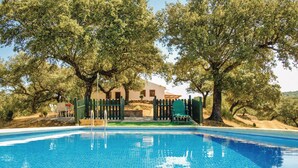 Una piscina rodeada de olivos, con una casa al fondo.