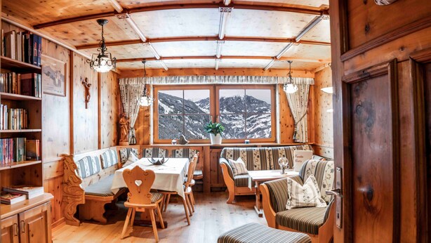 Een gezellig chaletinterieur met een eethoek, zitplaatsen, boekenkasten en uitzicht op een besneeuwde berg.