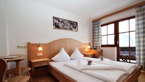 Een houten bed met witte lakens, twee nachtkastjes met lampen, een houten bureau en een raam met gordijnen.