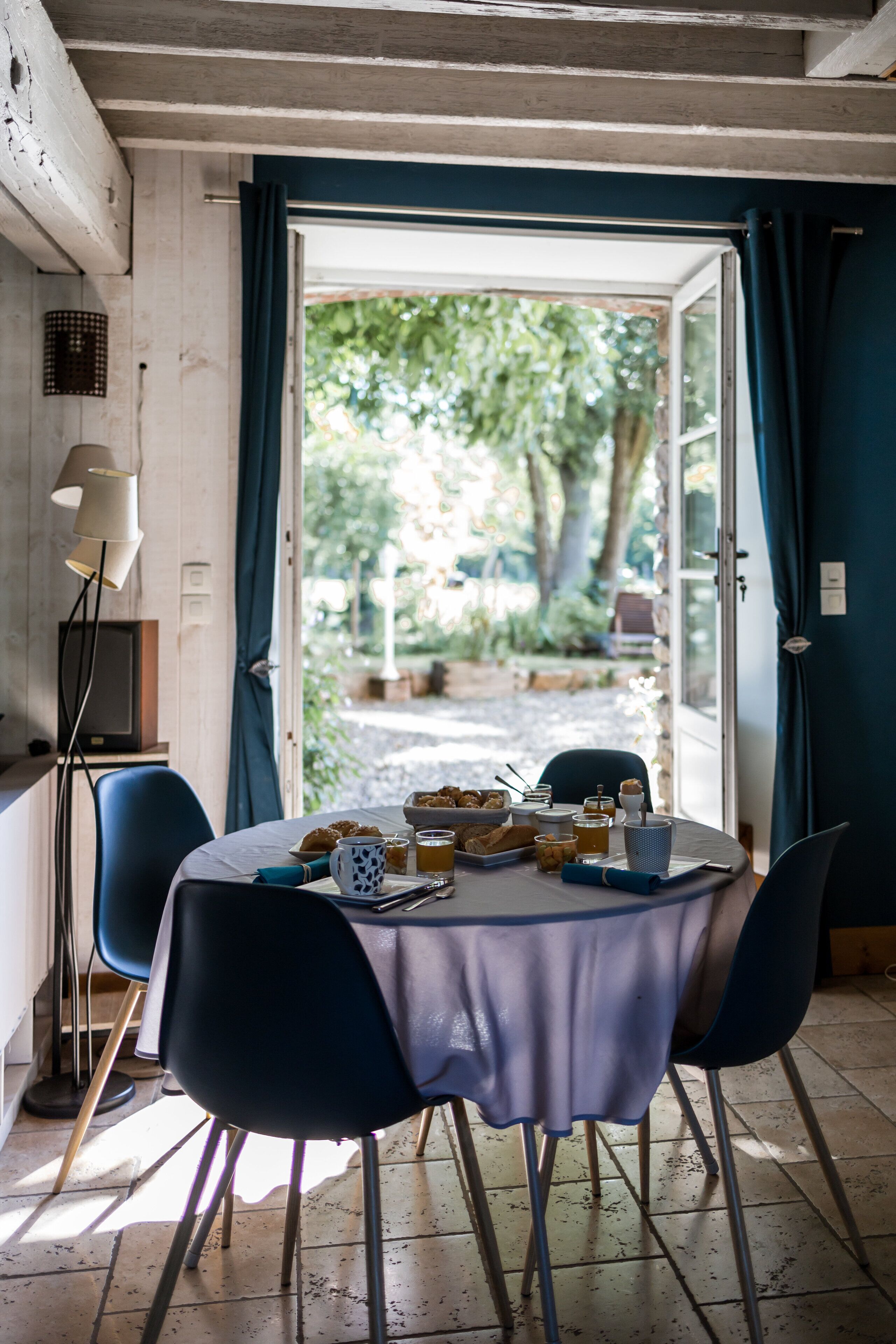 A dining area with a table set for two, a television, and a view of the garden through an open door.