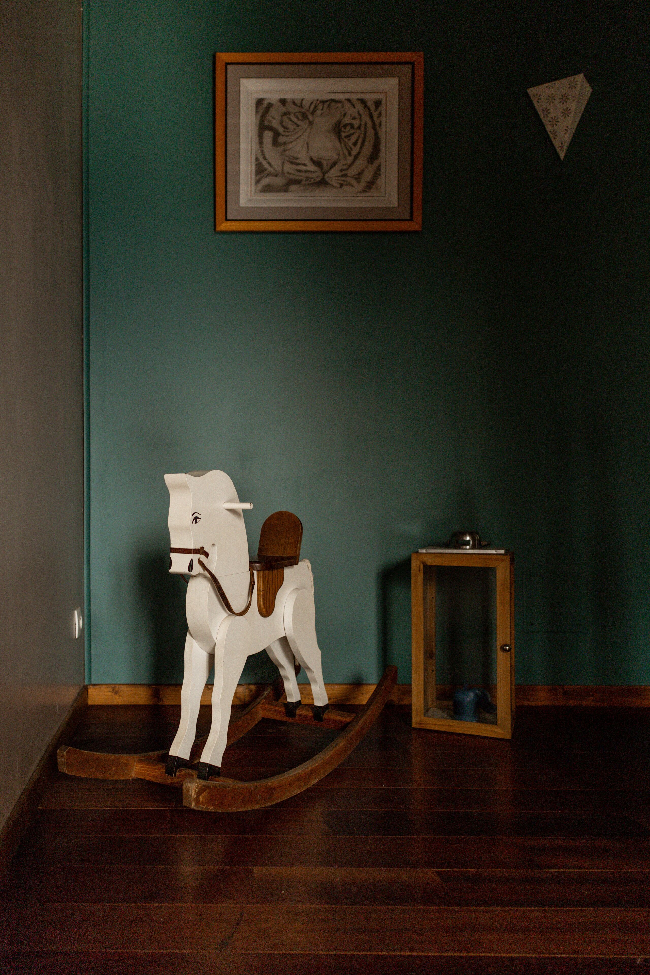 A room with teal walls, a wooden rocking horse, and a framed picture on the wall.